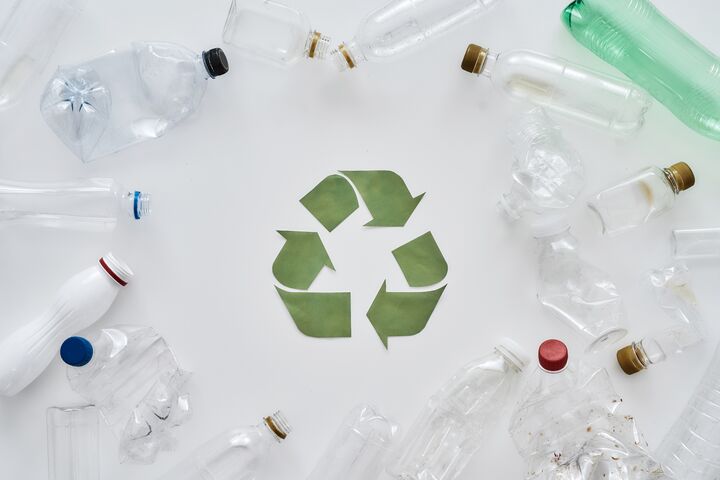 Flatlay composition with different empty plastic bottles and conceptual recycling sign made of paper in the center over white background. Sorting, recycling waste concept. Horizontal shot. Top view