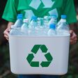 A woman collecting garbage and holding a recycle bin with plastic bottles in the outdoors