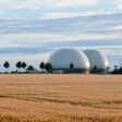 Biogas plant next to a yellow grain field. Summer sky with blue clouds. The evening sun lights up the gas storage tanks.