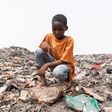 Despairing African child sitting on a garbage dump, looking at the plastic waste. Environmental justice concept.