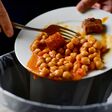 closeup of a young caucasian man throwing the leftover of a plate of chickpea stew to the trash bin