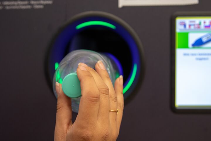 Junge Frau wirft leere Plastik Pflandflaschen in Automat. Automatisierte Leergutrücknahme