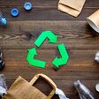 Green paper recycling sign among waste materials paper, plastic, polyethylene on dark wooden background top view.