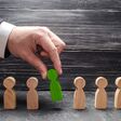 hand of a businessman takes a wooden figure of a man. The concept of search, hiring and firing workers, promotion. Business tactics and strategy, management, business management.