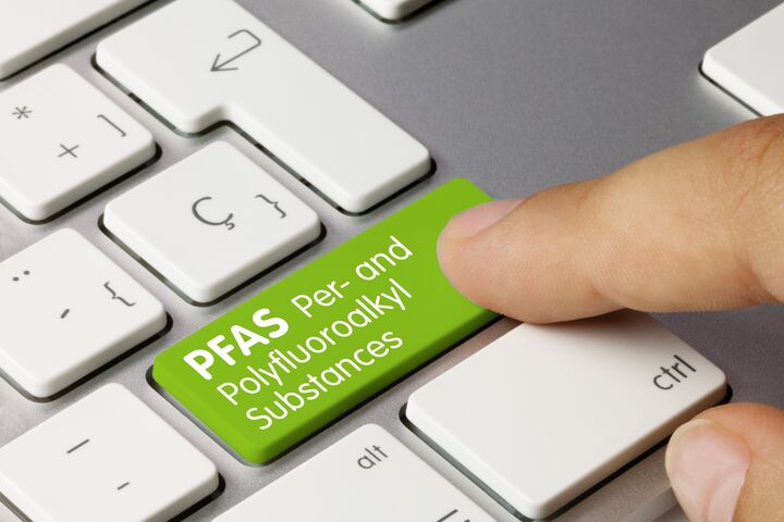 Per- and Polyfluoroalkyl Substances Written on Green Key of Metallic Keyboard. Finger pressing key.