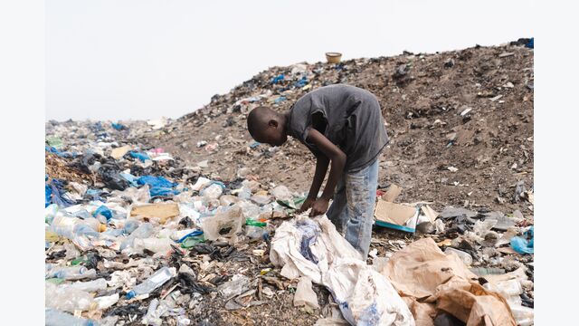 Joven recolector de basura africano llenando una bolsa de plástico con objetos reutilizables en un vertedero urbano; concepto informal de reciclaje de residuos