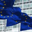 group of flags of the European Union waving in the wind in front of the European Parliament building.