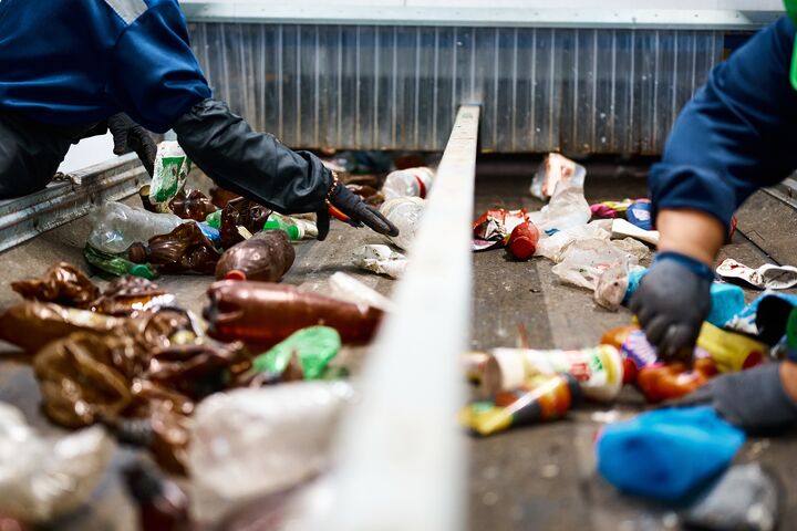 Worker in gloves sorts trash on conveyor belt in waste recycling plant workshop closeup. Plastic bottles reusing. Rubbish processing industry