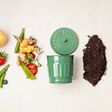 Green compost bin and kitchen leftovers. Recycling scarps, sustainable and zero waste lifestyle concept. Fruits and vegetable garbage waste turning into organic fertilizerd soil. Top view, flatlay