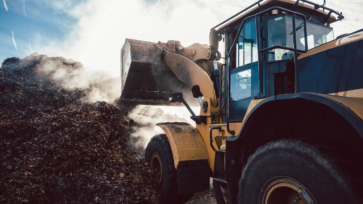 Earth mover working on pile of compost in industrial facility
