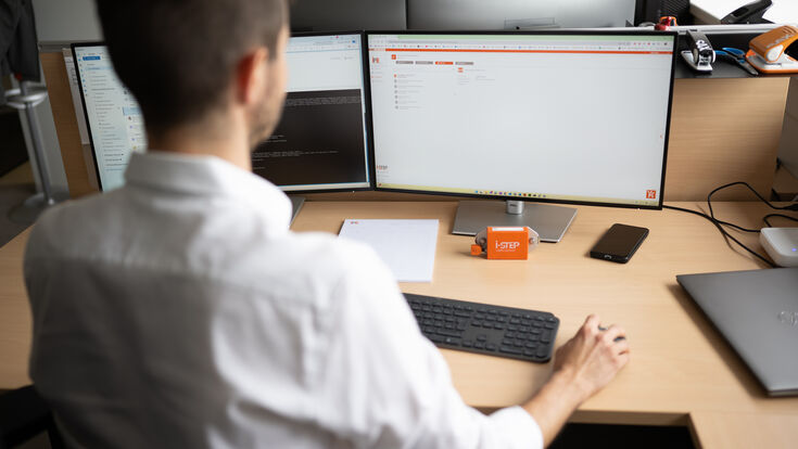Junger Mann sitzt vor Tastatur und Bildschirmen