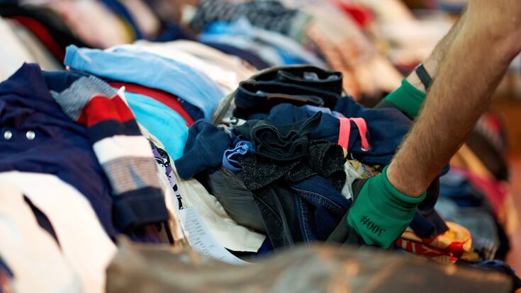 Person sorting second hand clothes by size and gender.