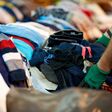 Person sorting second hand clothes by size and gender.