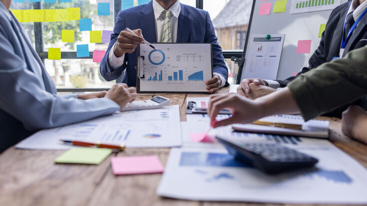 Group of confident business people point to graphs and charts to analyze market data, balance sheet, account, net profit to plan new sales strategies to increase production capacity.
