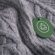A circular green tag with a recycling symbol hangs from on gray knitted fabric. Concept of sustainable development, textile recycling, and conscious consumption in fashion. High quality photo